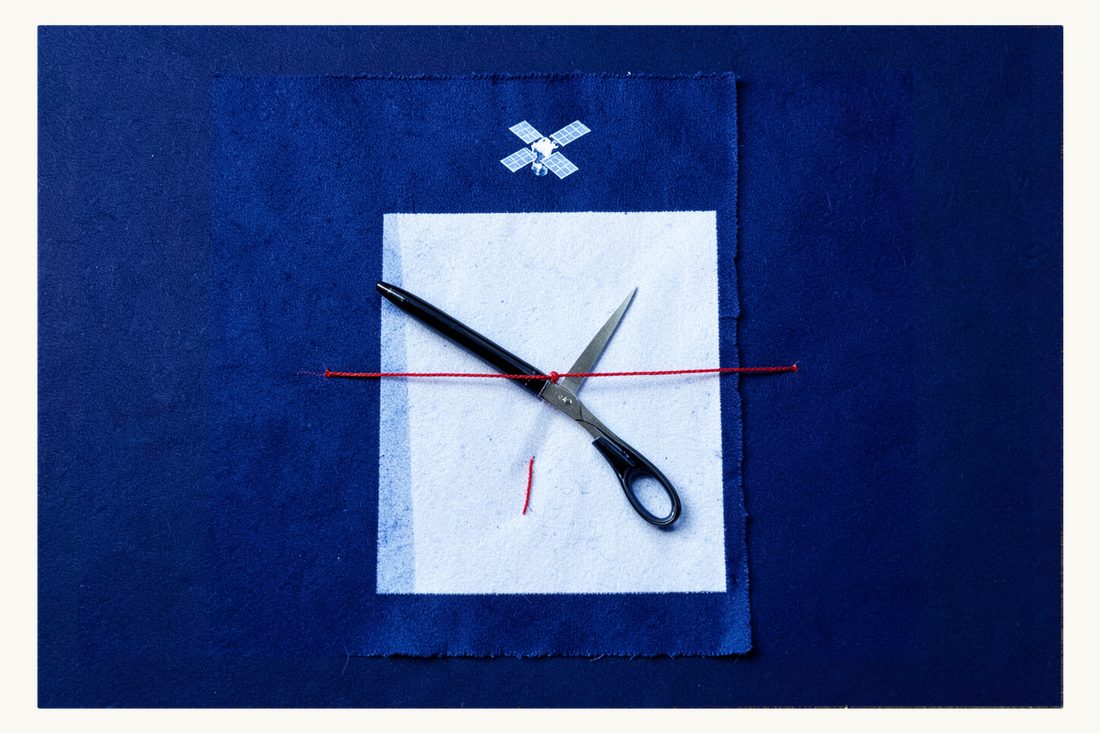 Failed diplomacy over military uses of outer space: a sheet of paper with a fountain pen, its red thread just cut by open scissors, a small satellite floating above, cyanotype print