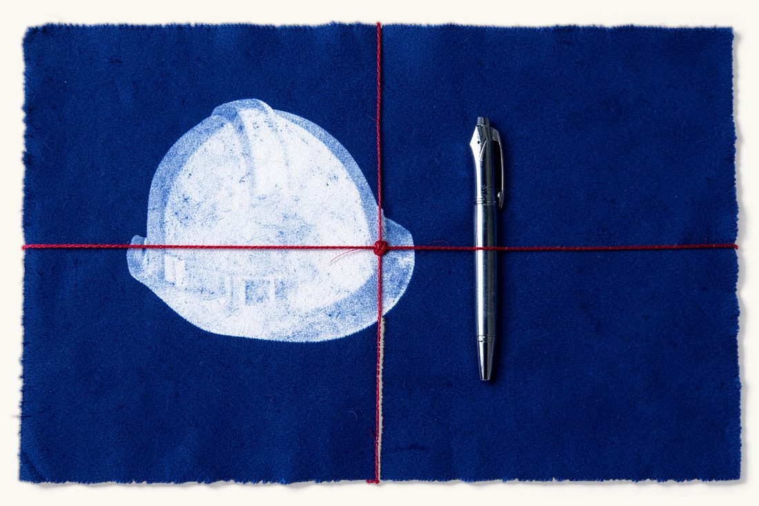 Construction contracts and FIDIC-style forms: a plain hard hat resting on a blank contract sheet with a fountain pen, tied together by a red thread, cyanotype print