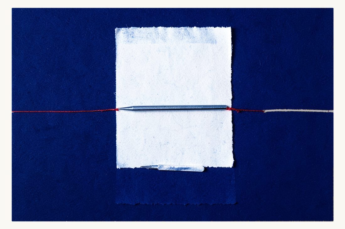 Informed consent before surgery: a large blank sheet with a fountain pen lying across it, the red thread running from the pen nib to a small scalpel below, cyanotype print